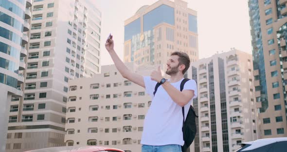 A Young Man with a Backpack Takes a Selfie in the City alt