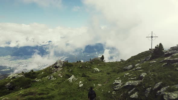 Aerial drone shot of a grass covered mountain top with a person hiking along a small trail. A valley alt