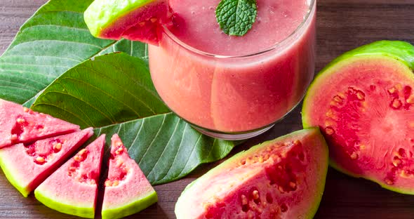 Glass of red guava juice and sliced guava slice on wooden background alt
