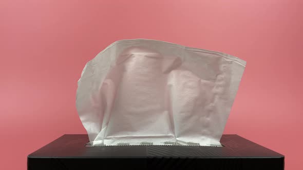 A person's hand pull out a piece of tissue from tissue paper box isolated on pink background.
