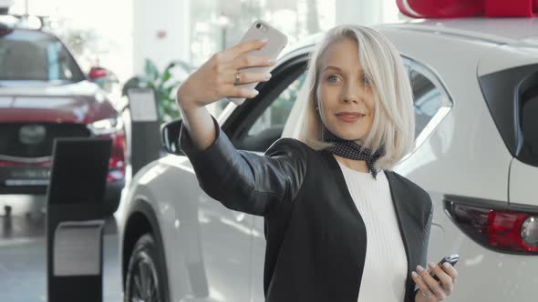 Happy Woman Taking Selfies with Keys To Her New Car at the Dealership
