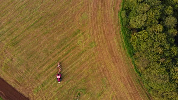 Drone fly above farm field where farmer driving a red tractor on the field alt