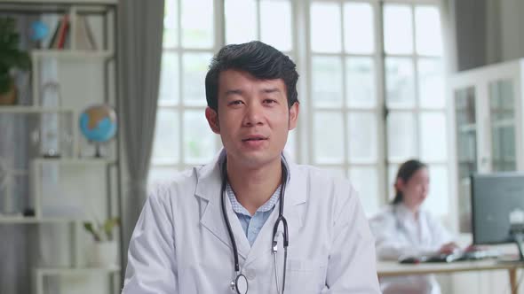 Asian Male Doctor Physician In White Medical Uniform Speaking Looking At Camera Make Video call alt