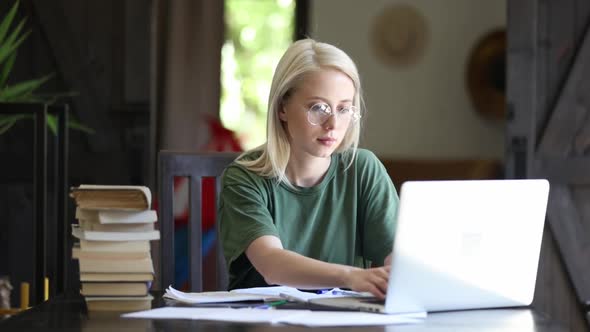 Blonde girl in glasses working with notebook at home as freelancer