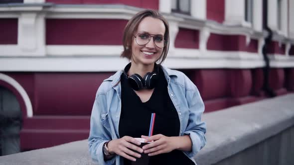 Gorgeous View of a Young Beautiful Girl in Glasses Standing with a Red Classic Building on the alt
