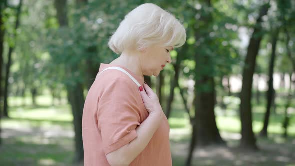 Side View of Senior Retiree Stopping in Sunny Park Because of Pain in Chest. Camera Approaches To alt