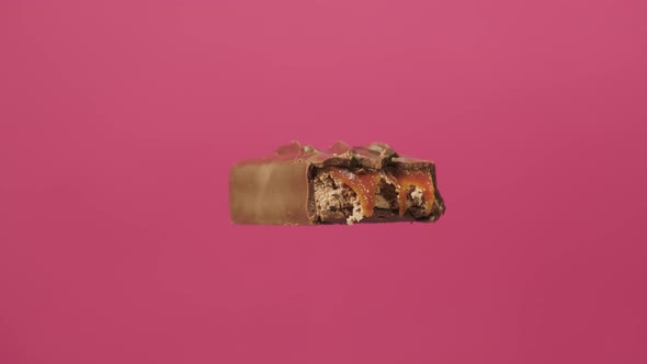 A Delicious and Unhealthy Chocolate Bar Rotates on a Pink Background. Bitten Sweets Isolated. The alt