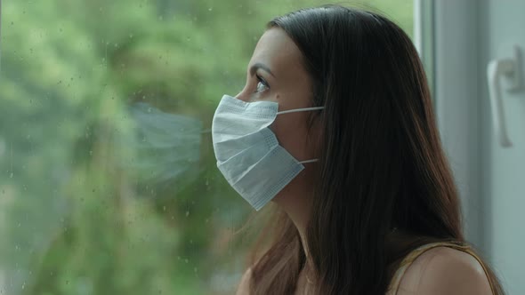 Woman in Face Mask Looks Through the Window alt
