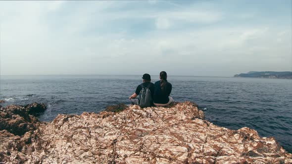 Couple in Love Sitting on a Rocky Edge By the Sea, Talking on Different Topics and Enjoy the View alt
