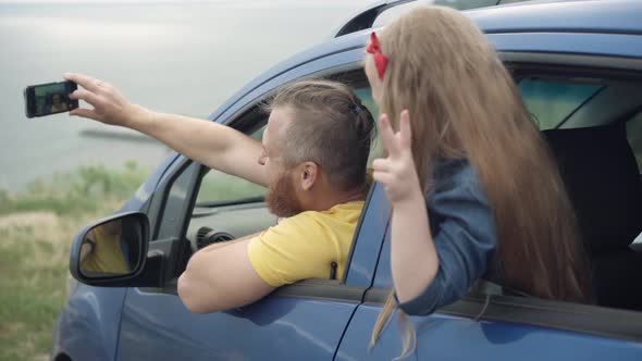 Positive Happy Excited Little Girl and Young Man Taking Selfie Sticking Out Car Window on River Bank alt