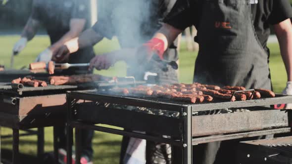 Two men baking some meats on heavily glowing grids and rotate them. alt