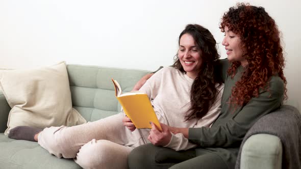 Latin Gay Women Couple Reading a Book Wearing Pajamas in Sofa at Home ...