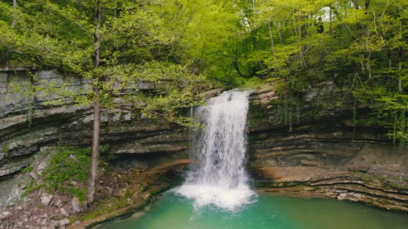 Stunning Scenery of a Small Waterfall and a Green Lake in the Forest Scenic Drone Shot alt