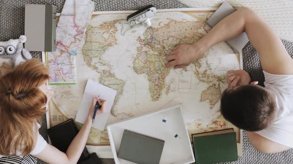 Man and Woman Planning Vacation Using a World Map and Other Travel Accessories alt