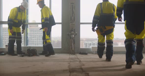 Tired Team of Builders Sitting on Heaters and Resting at Construction Site alt