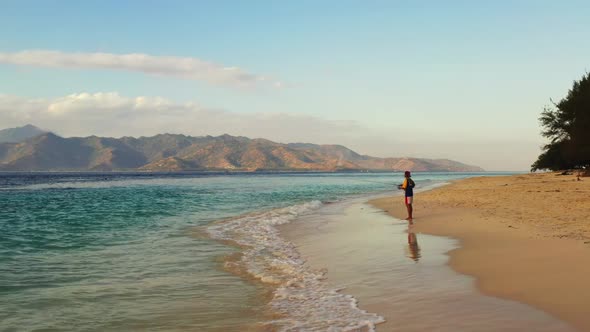 One man fishing alone on idyllic seashore beach holiday by turquoise sea with white sandy background alt