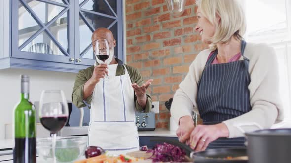 Mixed race senior couple wearing aprons talking while cooking together in the kitchen at home alt