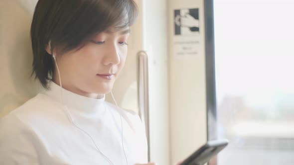 Portrait of attractive smiling asian woman holds the handrail and using smartphone for chatting