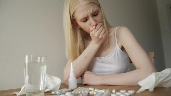 A Sick Woman Sits at Home with a Bunch of Pills Coughs and Blows Her Nose Into a Napkin