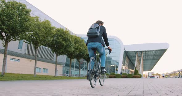 Office Worker with Backpack Riding a Bike on Cobbled Street alt