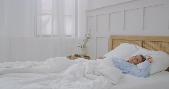 Happy Beautiful Woman Wake Up, Smiling and Stretching Her Arms in Her Bed in the Bedroom. Young alt