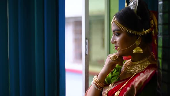 Newly wed Romantic and beautiful Indian bride looks outside through window on rainy evening alt