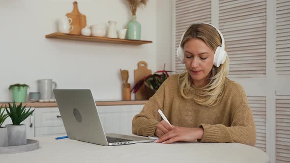 Young Woman in Big White Headphones Conference Calling on Laptop Talks with Online Teacher Studying alt