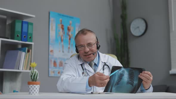 Senior Male Doctor Wearing Headset Videoconferencing Remote Patient Consulting About Corona Virus