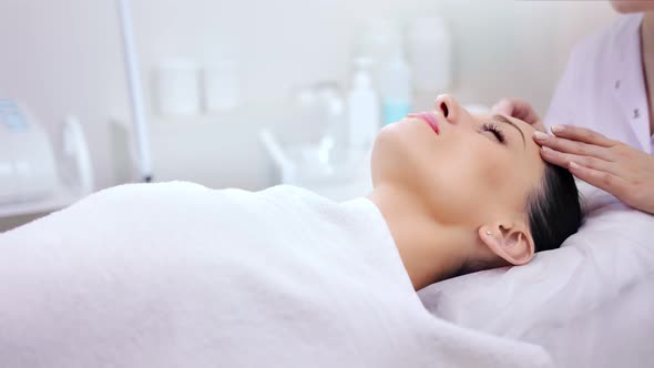 Medium Shot Caring Female Beautician Making Facial Massage to Young Adorable Client By Hands alt