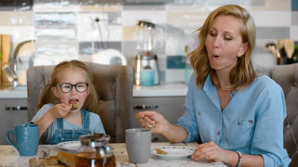 Young Mother and Little Daughter are Eating Meal and Talking at Table in Home Kitchen Rbbro alt