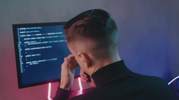 Back View Portrait of Tired IT Professional Programmer in Glasses Is Overworking on Computer alt