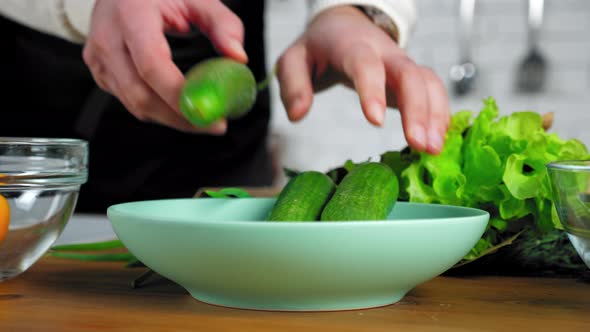 Close up chef man hands put fresh food cucumbers in plate at home kitchen alt