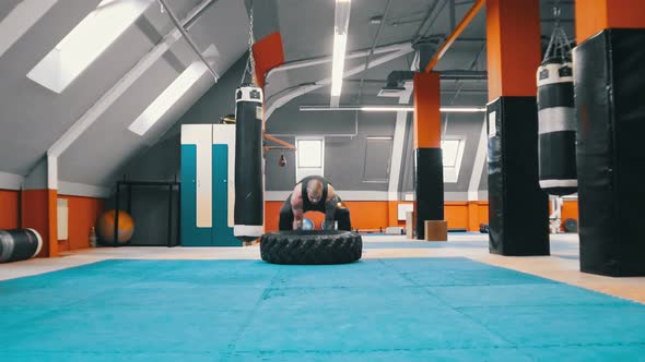 A Man Bodybuilder Flips a Tire on the Floor Over and Over alt