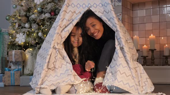 Black Mother and Daughter Hide in Play Wigwam with Garland alt