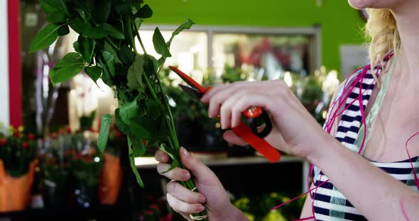 Smiling female florist trimming flower stem in flower shop alt