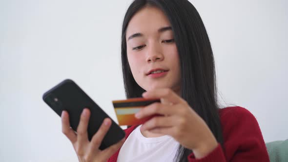 Beautiful Asian woman sitting sofa in the living room shopping online with credit card	