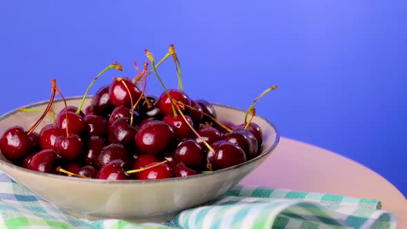 A Plate of Fresh Cherry Berries on a Blue Background Rotates Closeup