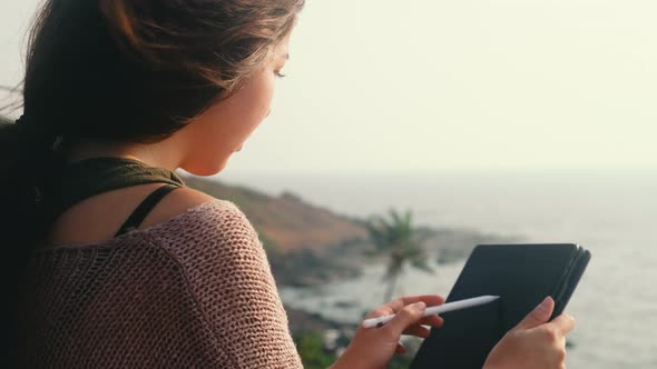 Young asian woman using digital tablet for drawing, sketching art design while sitting at hill alt