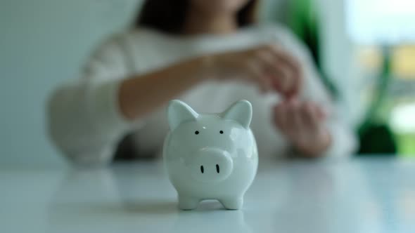 Closeup of a woman putting coin into piggy bank for saving money and financial concept