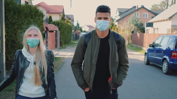Multiethnic Man and Woman in Medical Masks Walking Down the Street in Housing Estate alt