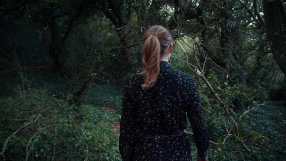 Woman Walking Along Forest Path with Dead Tree Branches Sticking Out alt