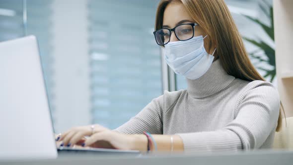 Woman Working at a Laptop in Protective Mask Typing Text in the Office Employee at Work on the alt