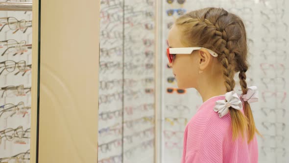 Cute Little Girl Choosing Sunglasses From the Display at the Shopping Mall alt