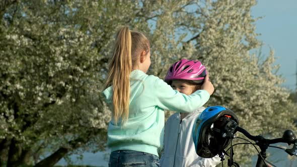 Children learn to ride bicycle in a park on spring day. Teenager girl helping preschooler girl