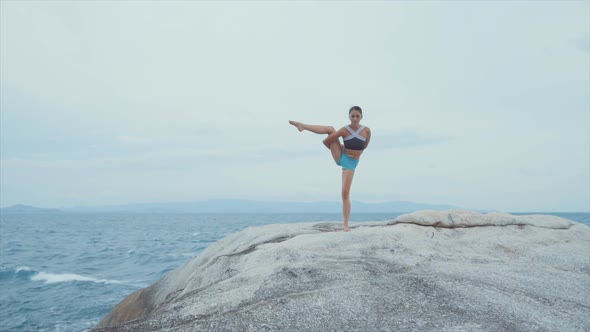 Woman Standing on One Leg and Meditating on Rocks Near Ocean alt