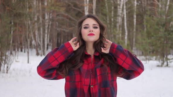 Young Woman with Wavy Hair Standing and Touching Face in Winter Forest