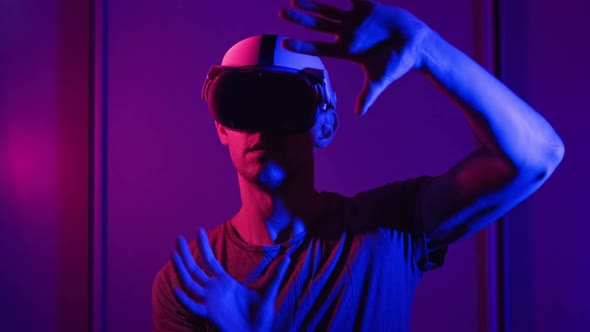 Man in a Virtual Reality Helmet Illuminated in Red and Blue Plays a Game alt