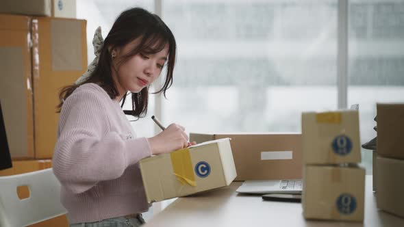 Asian woman packing products in boxes and writing envelopes to send to customers, online selling