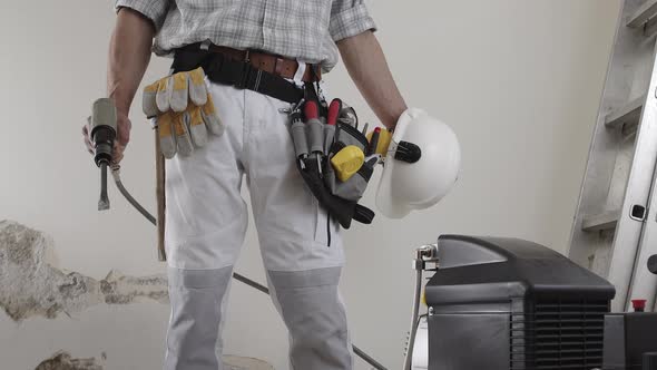 construction man worker wearing a tool bag belt, helmet with headphones and pneumatic air hammer