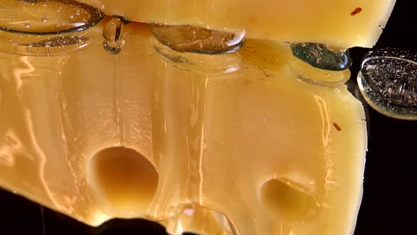 Drops of honey flow down from the cheese on a mirrored black background. alt